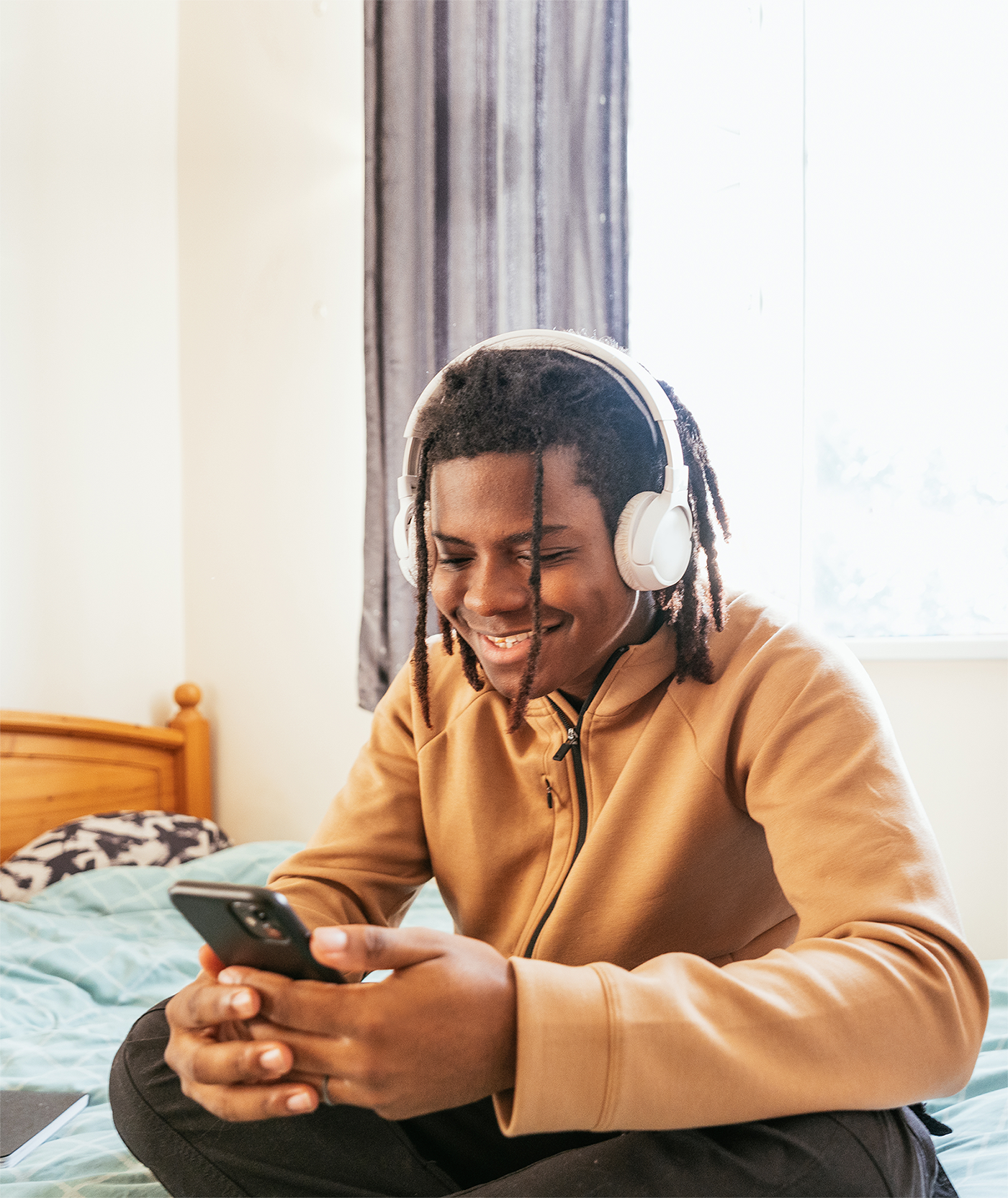 Teenager in bedroom using smart phone and wireless headphones