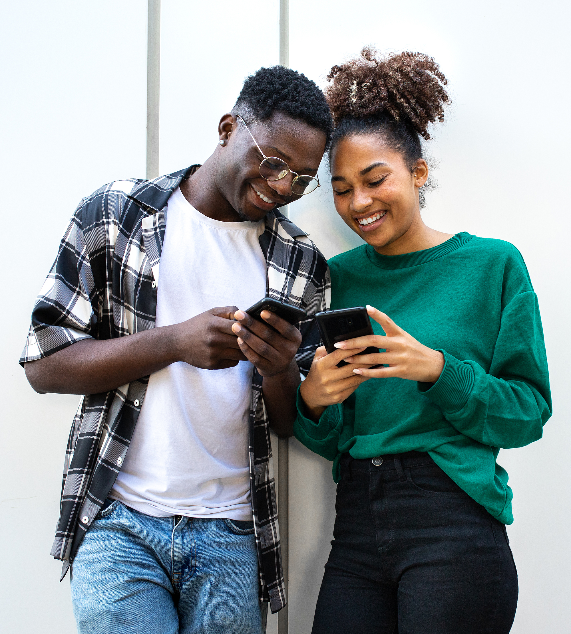 African American young couple looking smart phones together standing against white wall